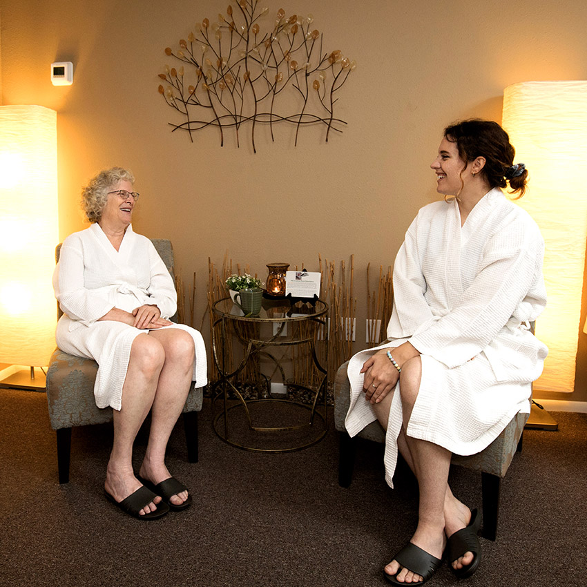 Two woman wearing a white robes while sitting in the relaxation lounge at Natural Balance Massage Therapy & Wellness Center in Palm Harbor, Florida.