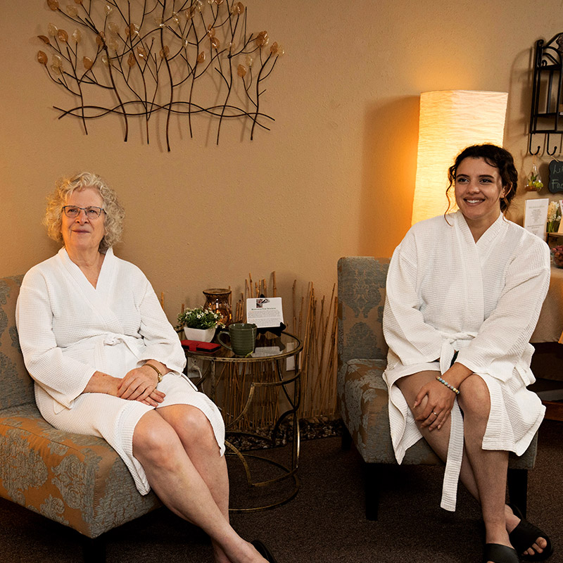 Two woman wearing a white robes while sitting in the relaxation lounge at Natural Balance Massage Therapy & Wellness Center in Palm Harbor, Florida.