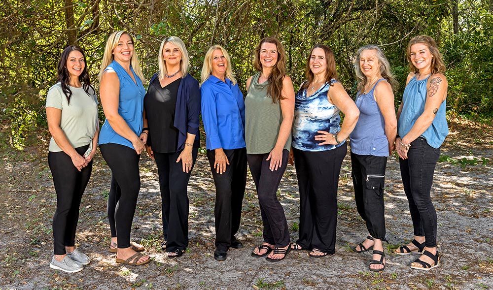 The Natural Balance Massage Therapy & Wellness Center team posing for a group photo outside next to the trees by their location in Palm Harbor, Florida.